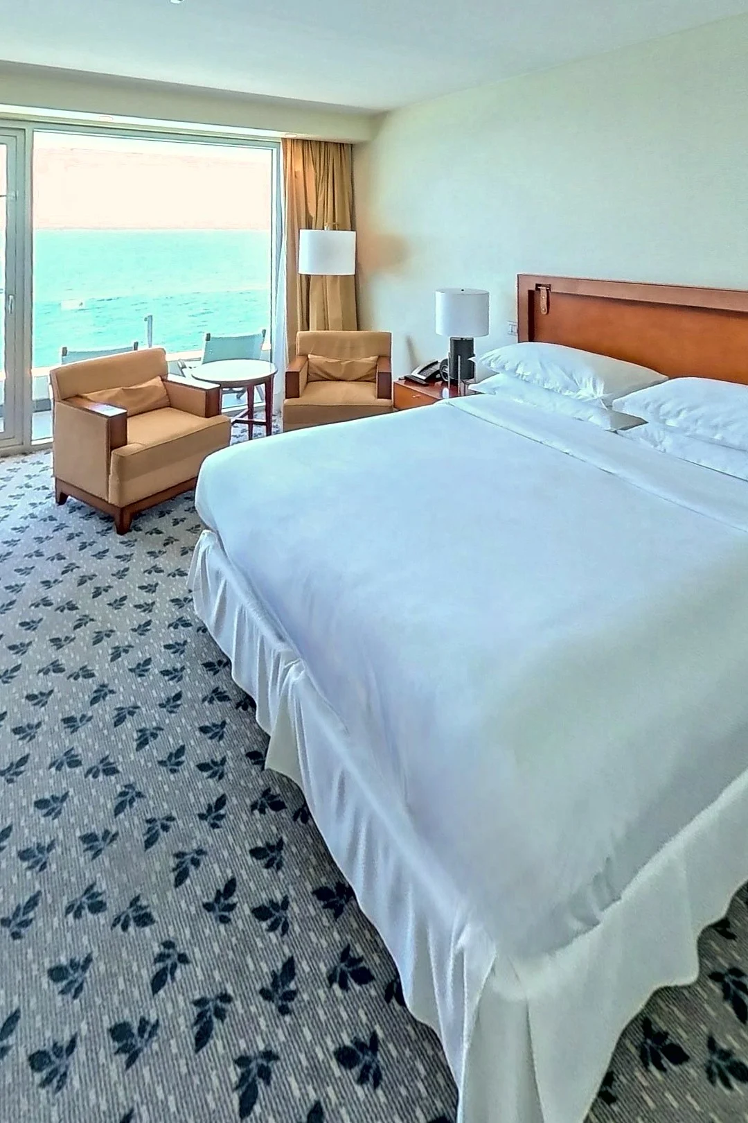 A sea-view hotel room: the king bed, the armchairs and the sea through the window