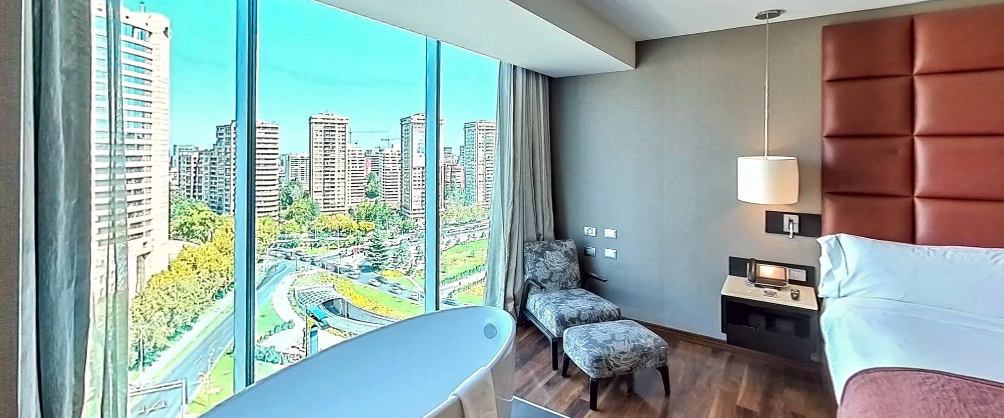 A suite's bedroom: a freestanding bathtub by the window, the bed and the city below