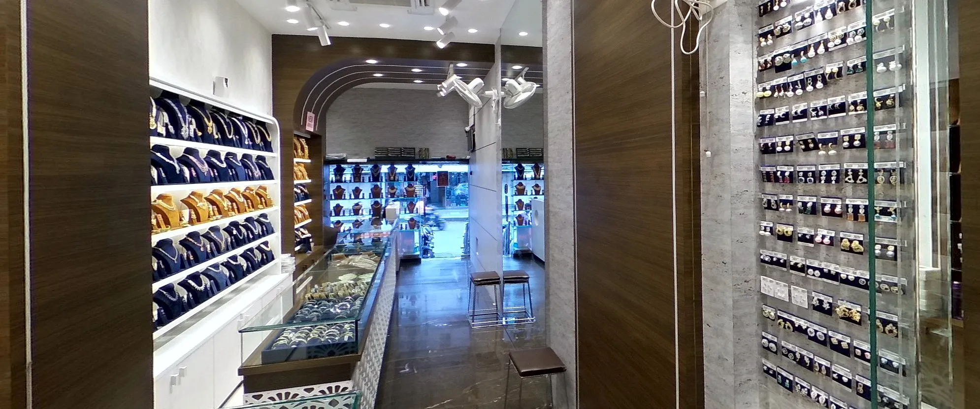 A jewellery store's centre counter: a lit wall of sets above a glass case of bangles